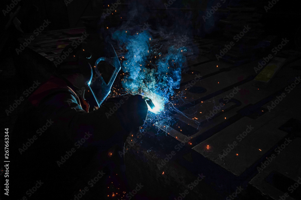 The working welder performs welding work in production using electric arc metal welding.