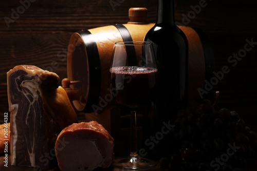 Still life in a rustic style. Grapes on a wooden table with a bottle of wine and meat and cheese. Antipasto and red wine