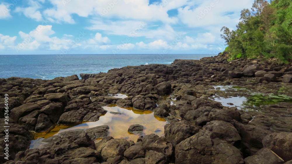 Rocky coast, water pools and blue pacific ocean at Queen's Bath, Kauai, Hawaii, USA