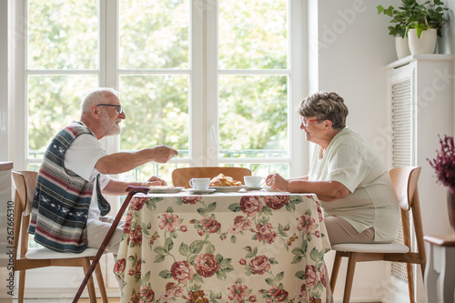 Senior couple sitting together at table drinking tea and eating cake