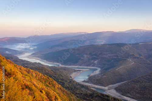 Autumn scene from viewpoint Goat rock with soft view of meandering lake Zavoj during misty, moody sunrise
