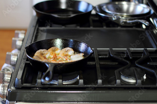 Shrimp cooking in butter and garlic in a cast iron skillet on the  stove.