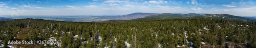 wide panoramic landscape of Jizera Mountains jizerske hory, view from peak of holubnik mountain with lush green spruce forest, trees, hills and fields springtime with snow remains, blue sky background
