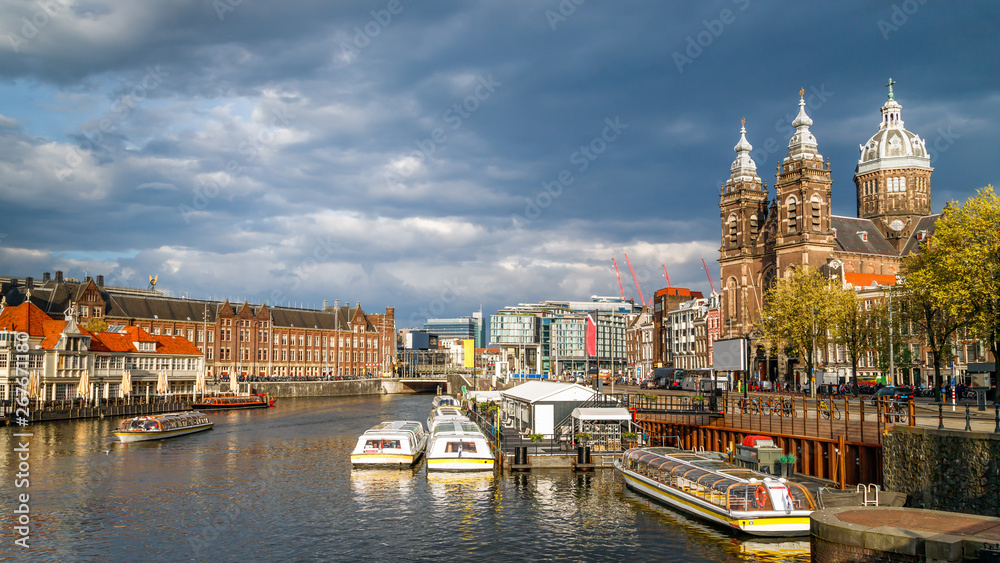 Amsterdam, Netherlands. City skyline. View of Central Train Station, canal with boats, Basilica of Saint Nicholas in the old center district.