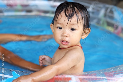 In the summer season. Asian happy baby child girl playing and swimming in a plastic water pool with her young brother.