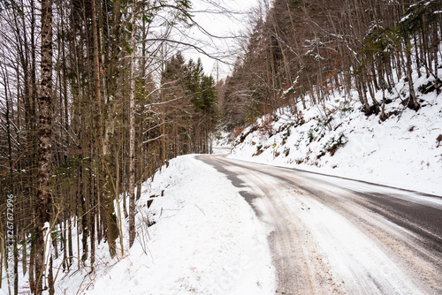 Snowy Forest Road in the Alps on a cloudy winter day. Concept of dangerous driving conditions.