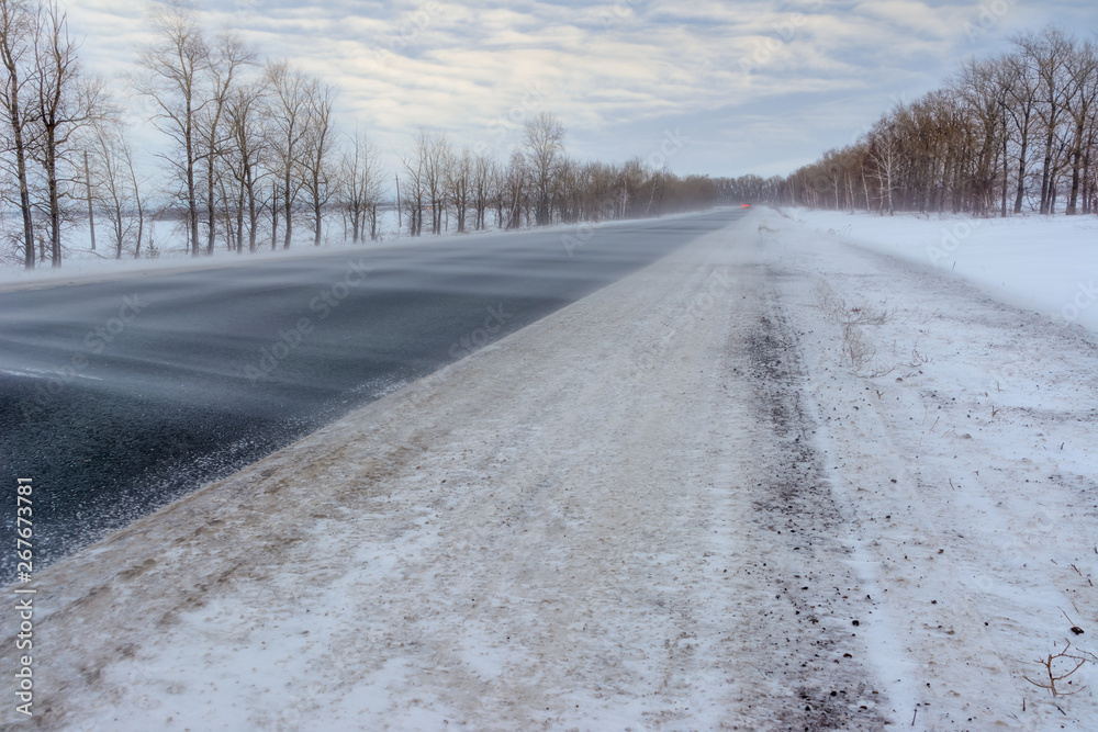 Fototapeta premium Snowstorm on the highway. Patterns on the winter highway in the form of four straight lines. Snowy road on the background of snow-covered forest.