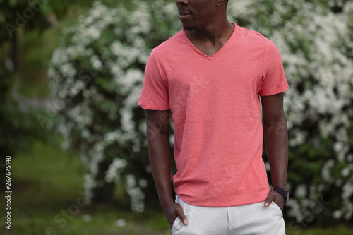 Unrecognizable African American man in living coral color empty t-shirt standing near bush outdoor, mockup