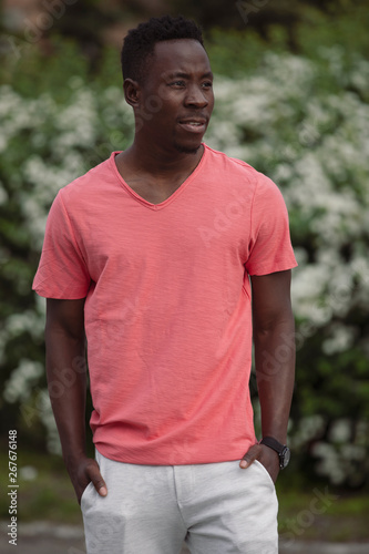 African american man in living coral color empty t-shirt standing near bush outdoor, mockup