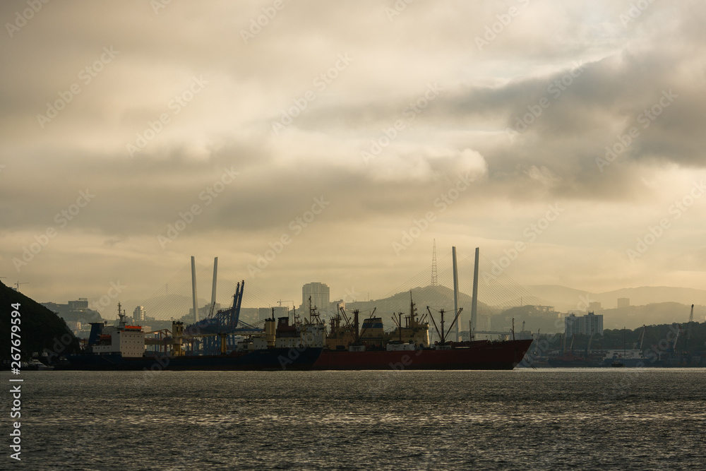 The sea trade port of Vladivostok on the background of the Golden Bridge across the Golden Horn Bay in the rays of the rising sun The sea trade port of Vladivostok on the background of the Golden Bridge across the Golden Horn Bay in the rays of the rising sun