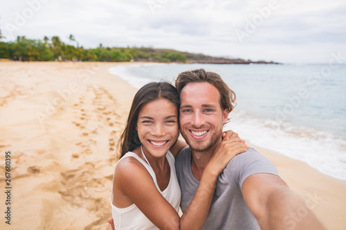 Two friends taking self portrait picture with phone. Smiling young interracial couple taking selfie on vacation travel. Asian woman, Caucasian man. Two young adults happy.