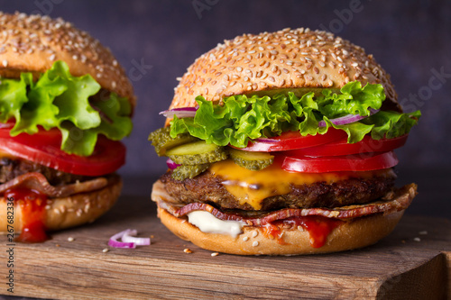 Two delicious homemade beef burgers with bacon on wooden chopping board