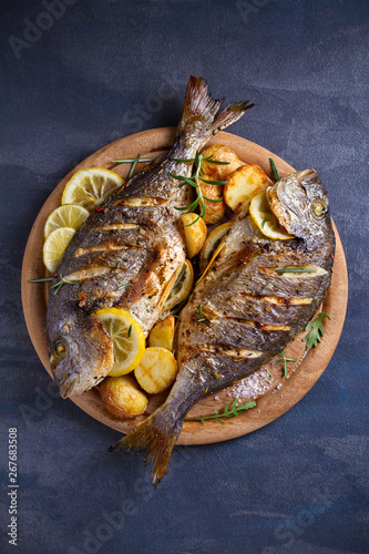 Roasted fish and potatoes, served on wooden tray. overhead, vertical - image