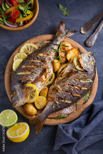 Roasted fish and potatoes, served on wooden tray. overhead, vertical - image