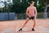 Young man runner stretching his leg on race track in stadium