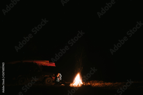 Woman sitting and getting warm near the bonfire in the night forest.