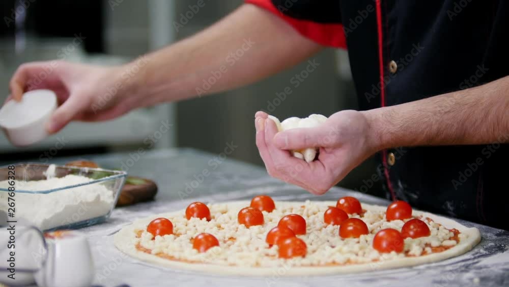 Restaurant kitchen. A chef putting special large pieces of cheese on the pizza Restaurant kitchen. A chef putting special large pieces of cheese on the pizza