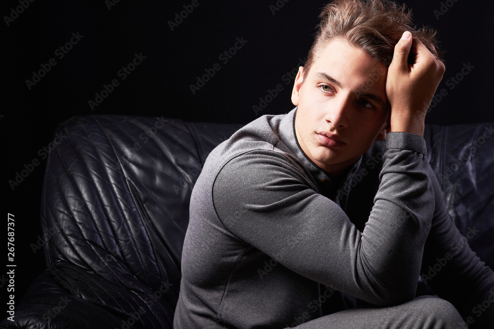 Fashion portrait of elegant young man sitting on leather sofa on black background Fashion portrait of elegant young man sitting on leather sofa on black background