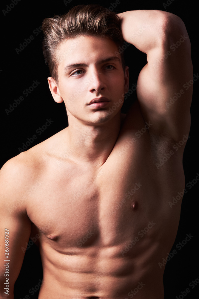 Studio portrait of handsome muscular shirtless young man isolated on black Studio portrait of handsome muscular shirtless young man isolated on black