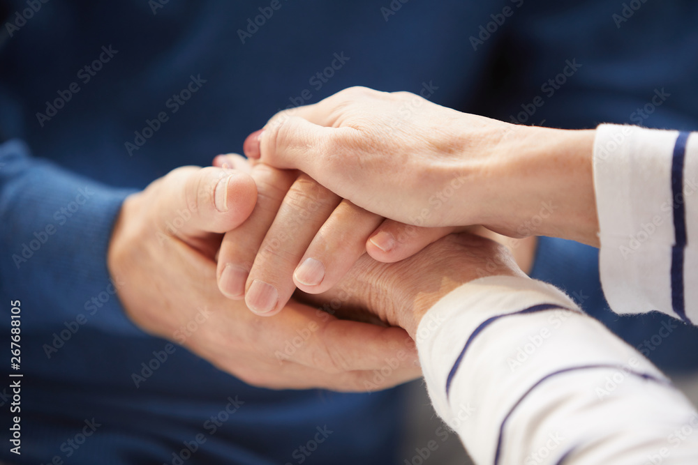 Close up of senior couple holding hands caringly against blue background, copy space