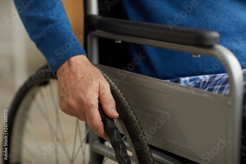 Close up of handicapped senior man pushing wheels of wheelchair, copy space