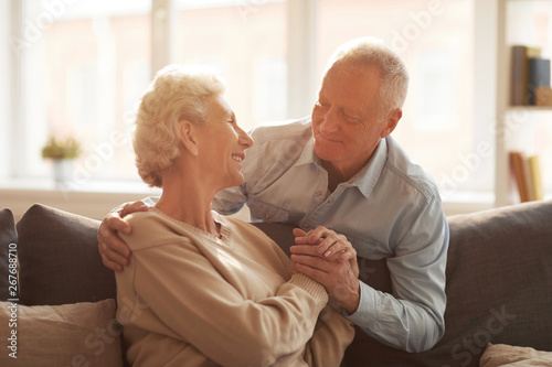 Portrait of loving senior couple looking at each other while posing at home lit by sunlight, copy space