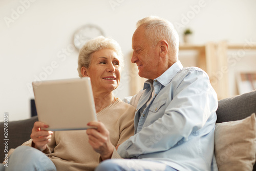 Low angle portrait of modern senior couple using digital tablet at home lit by sunlight, copy space