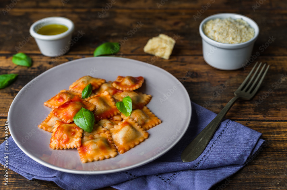 Ravioli stuffed pasta with tomato sauce and basil against dark wooden background