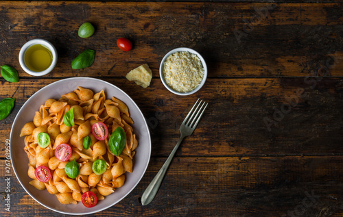 Conchiglie abissine rigate pasta with tomato sauce, cherry tomatoes, and basil against dark wooden background photo