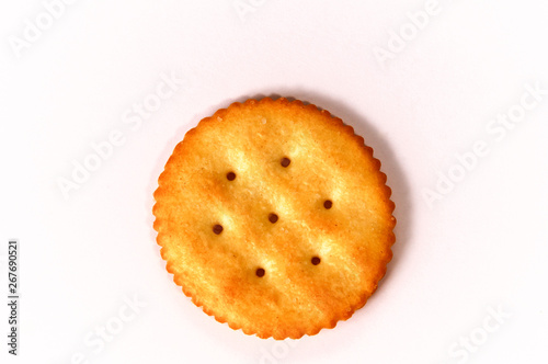 Top view of one round buttery cracker with holes and salt on white background.