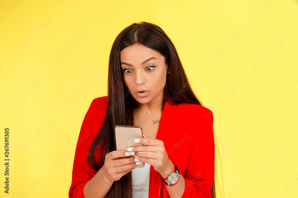 Shocked woman looking at mobile phone on yellow Shocked woman looking at mobile phone on yellow