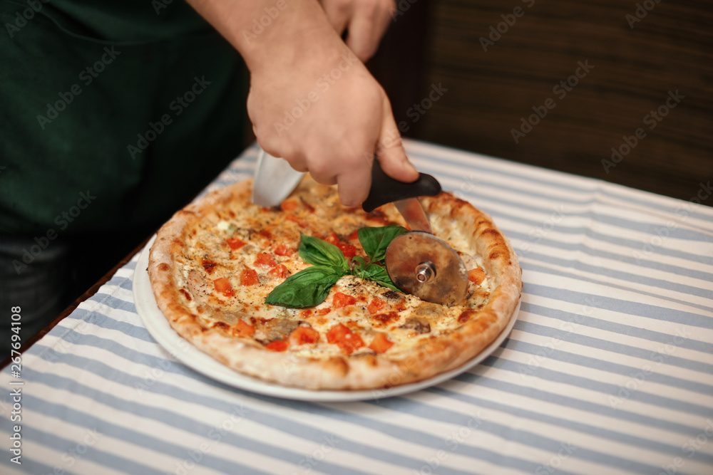 Man cutting tasty oven baked pizza on table, closeup