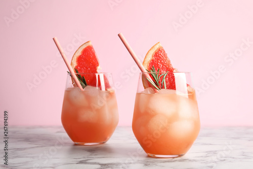 Glasses of grapefruit cocktail on table against color background photo