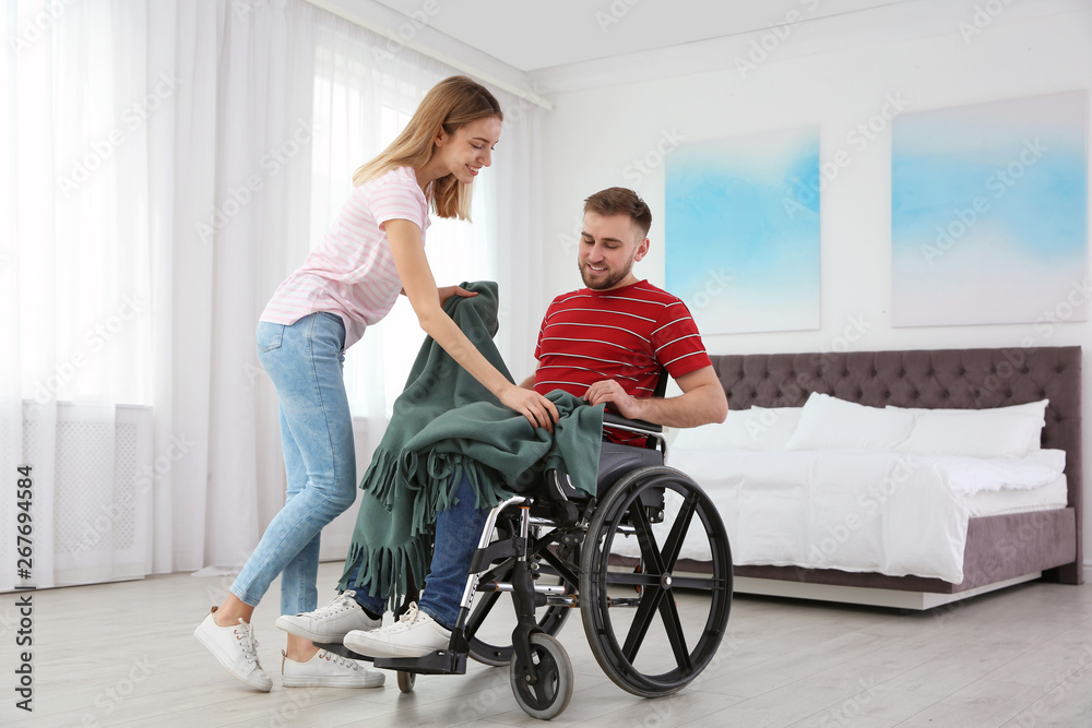 Woman covering man in wheelchair with plaid at home. Helping disabled Woman covering man in wheelchair with plaid at home. Helping disabled