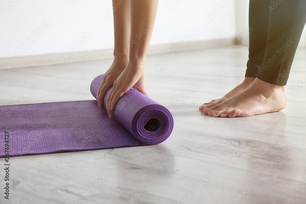 Woman rolling yoga mat on floor indoors, closeup Woman rolling yoga mat on floor indoors, closeup