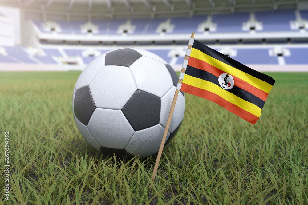 Naklejka premium Ugandan flag in stadium field with soccer football