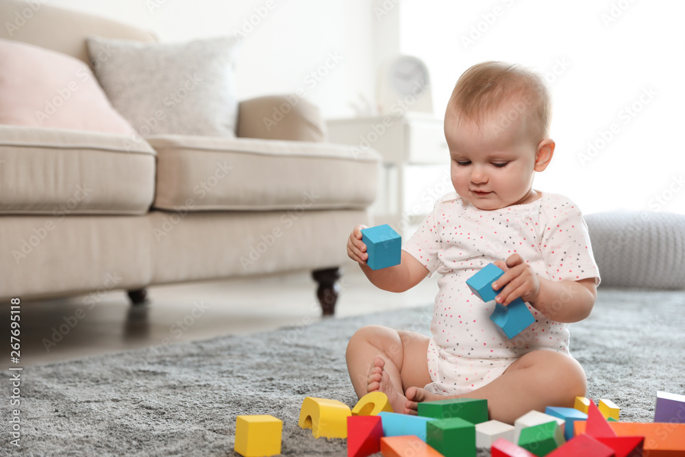 Cute baby girl playing with building blocks in room. Space for text Cute baby girl playing with building blocks in room. Space for text