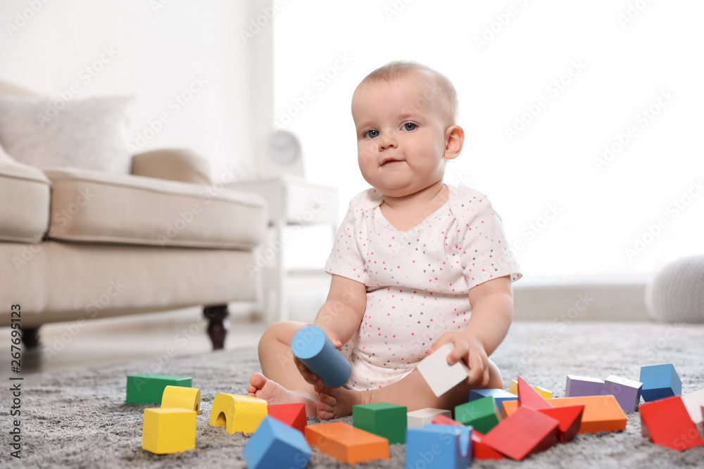 Cute baby girl playing with building blocks in room Cute baby girl playing with building blocks in room