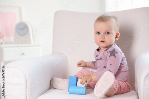 Cute baby girl playing with building blocks in armchair at home. Space for text
