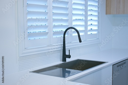Open plantation shutters and black kitchen sink mixer tap.