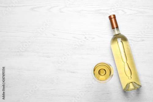 Glass and bottle with white wine on wooden background, flat lay. Space for text