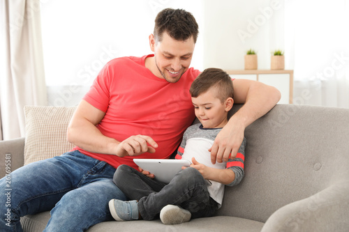 Boy and his father with tablet sitting on sofa at home. Family time © New Africa