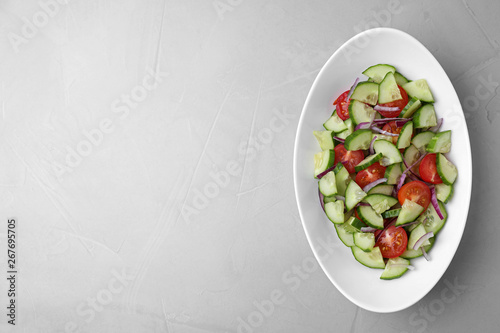 Plate of vegetarian salad with cucumber, tomato and onion on light background, top view. Space for text