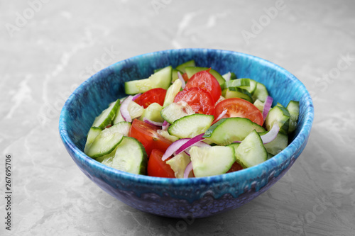 Bowl of vegetarian salad with cucumber, tomato and onion on table
