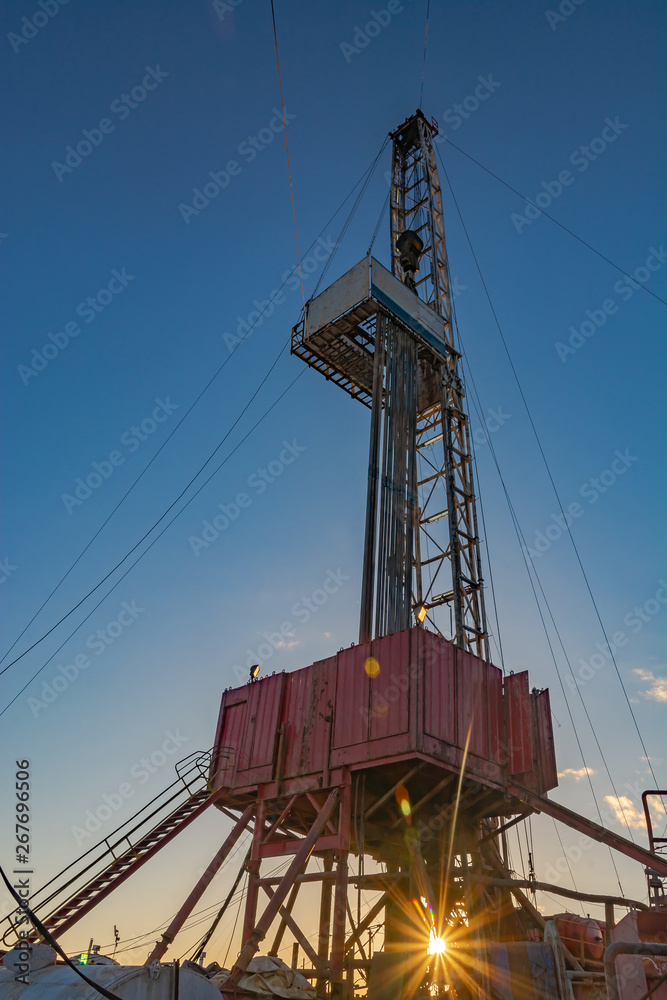 Drilling rig for deep drilling for oil and gas with a sunbeam at the base. The image of bursting energy of the subsoil. Many drill pipes installed vertically. Drilling rig for deep drilling for oil and gas with a sunbeam at the base. The image of bursting energy of the subsoil. Many drill pipes installed vertically.