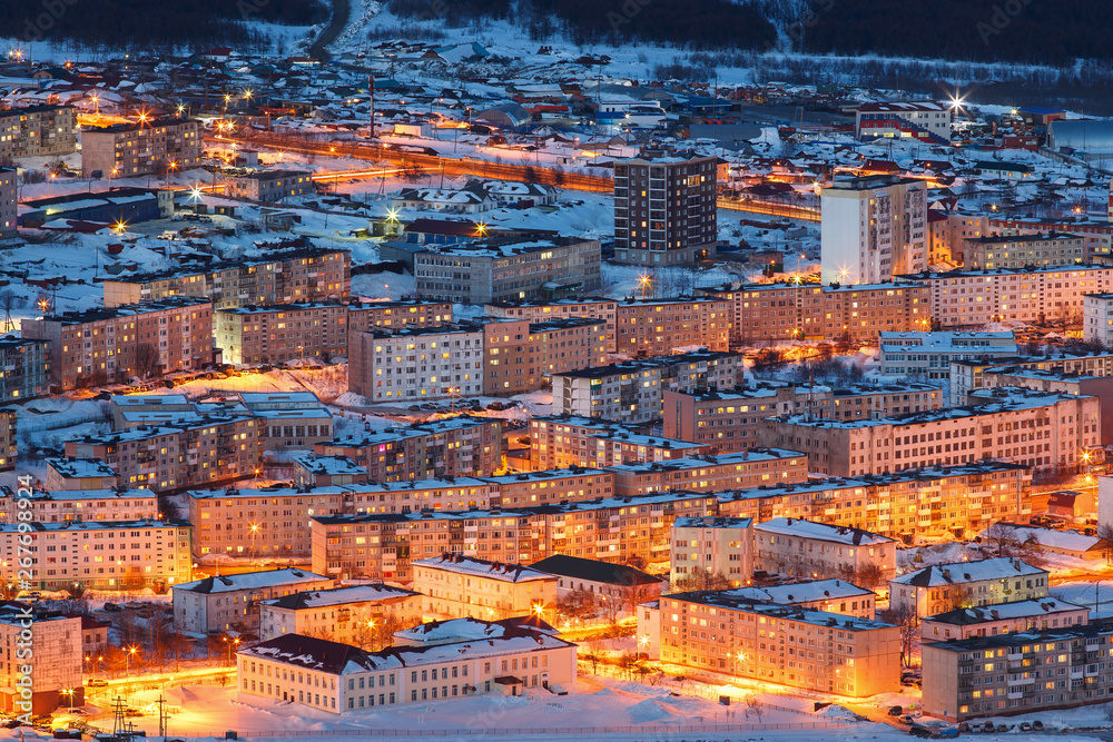 Aerial view of the night city. Cityscape with many buildings. Top view of the town with bright street lighting at dusk. City of Magadan, Magadan Region, Far East of Russia. Siberia.