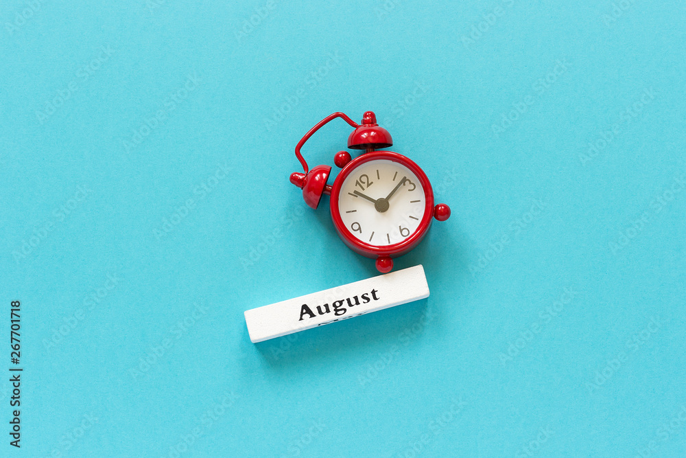 Wooden calendar summer month August and red alarm clock on blue paper ...