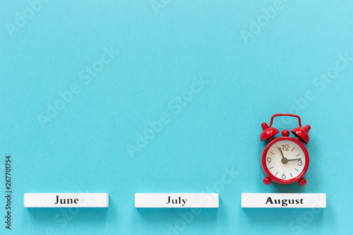 Obraz na plátně Wooden calendar summer months and red alarm clock over August on blue background