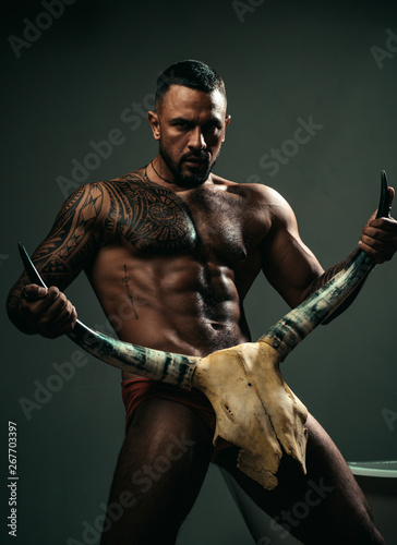 High testosterone level. Strong hispanic man full of testosterone and desire holding skull and horns. Fit latino man showing muscular body and six pack abs, testosterone. Potency and testosterone photo