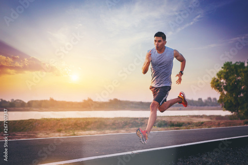 Silhouette of man running sprinting on road. Fit male fitness runner during outdoor workout with sunset background